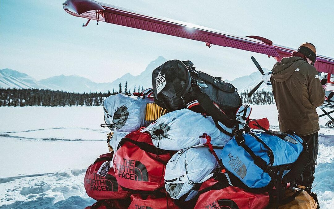 North Face Base Camp duffel bags stacked in the snow by an airplane